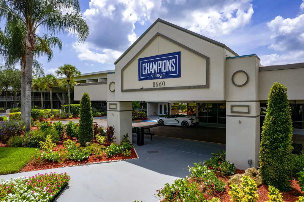 Main entrance of Champions Village with driveway, signage, and landscaped entryway